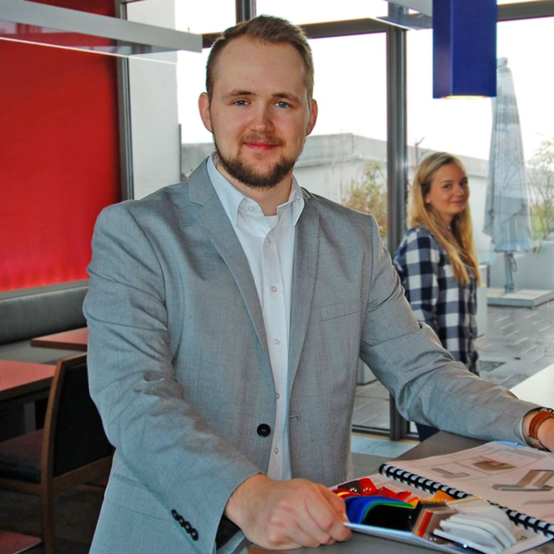 Zu sehen ist ein sympathischer Mann mit einer freundlichen Kollegin im Hintergrund. Sie stehen im Cafe eines Unternehmens für Lichtwerbung in Freystadt