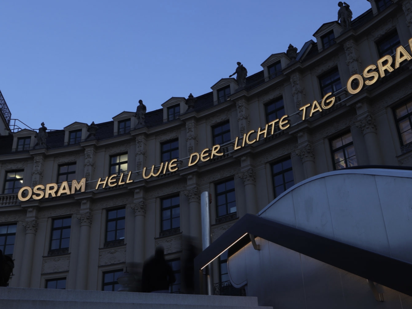 Leuchtende OSRAM-Werbeanlage in klassischem Stil an einem historischen Gebäude. Guttenberger & Partner haben diese Lichtinstallation entwickelt, um zeitlose Eleganz mit moderner Lichttechnik zu verbinden und so eine markante Außenwerbung zu schaffen.